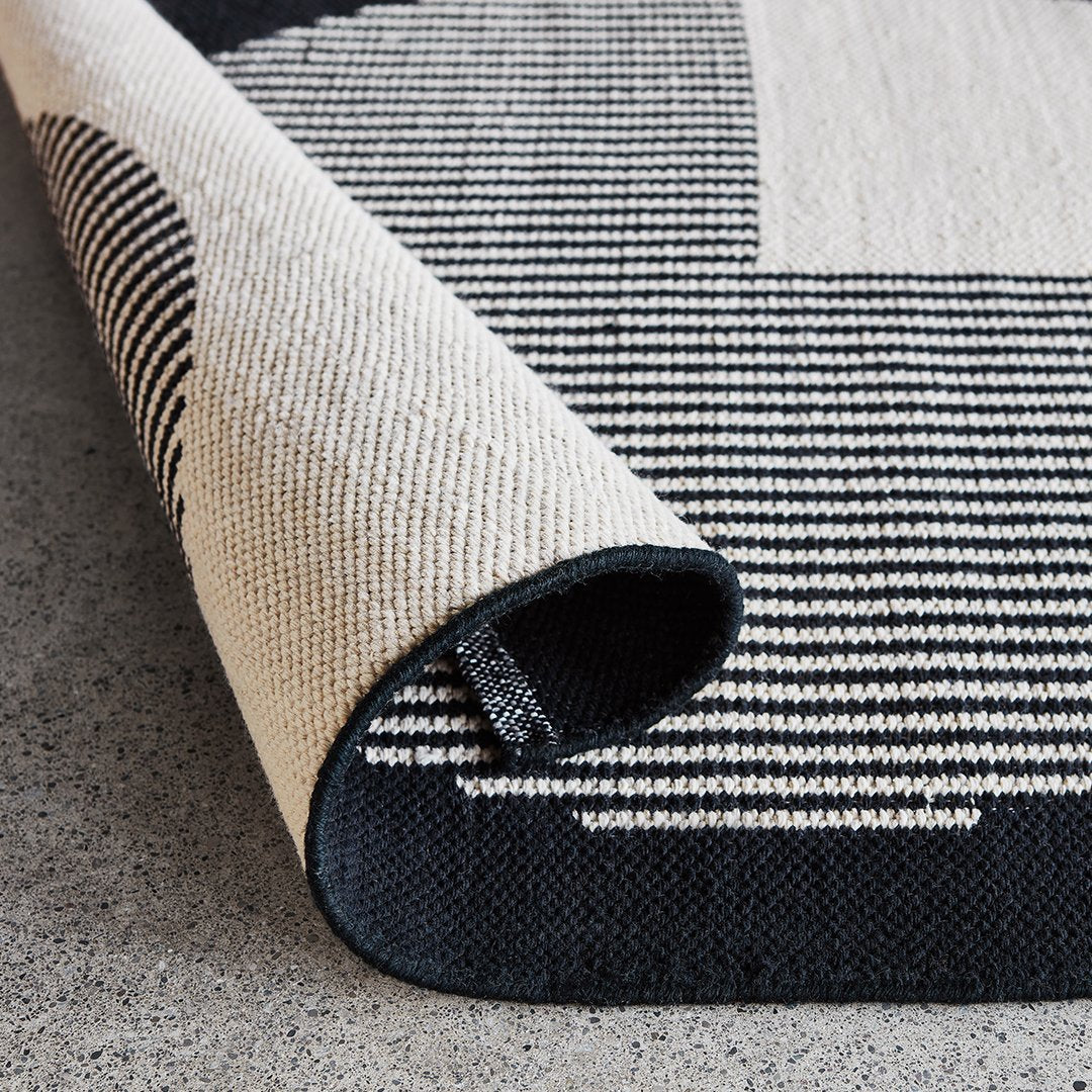 "Striped black and cream indoor rug with a textured design, showcasing a modern, minimalist aesthetic."