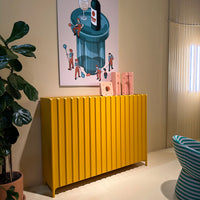 Bright yellow ribbed sideboard against a pastel wall, complemented by colorful artwork and green plant.