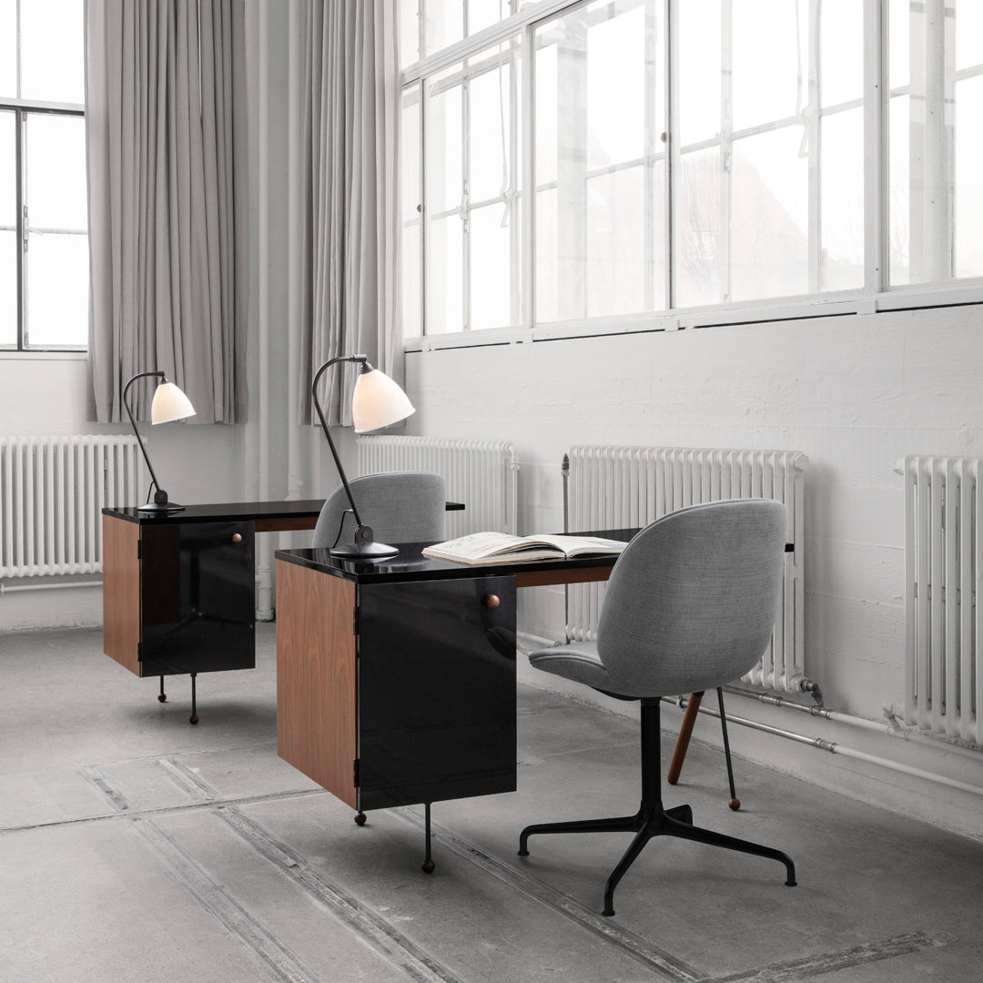 Modern desks featuring a black and wood finish, paired with gray upholstered chairs in a bright, minimalist workspace.