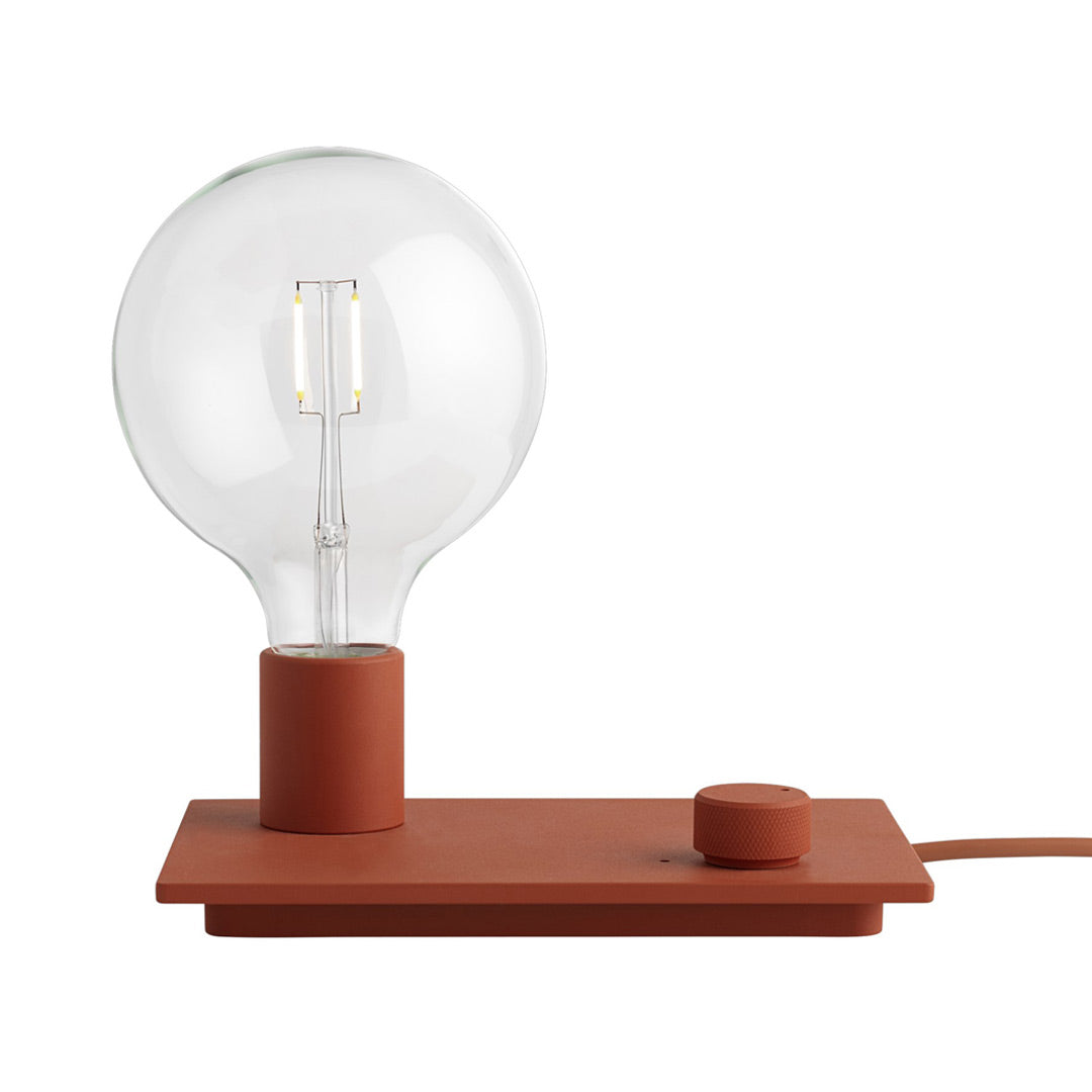 Rust-colored lamp with a smooth base and clear glass bulb, featuring a minimalist design.