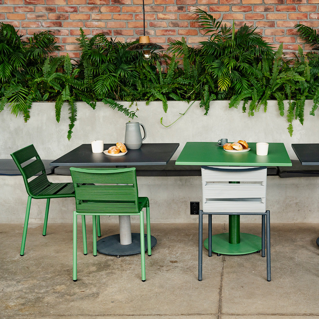Green and gray outdoor dining furniture featuring sleek lines and modern design against a brick wall backdrop.