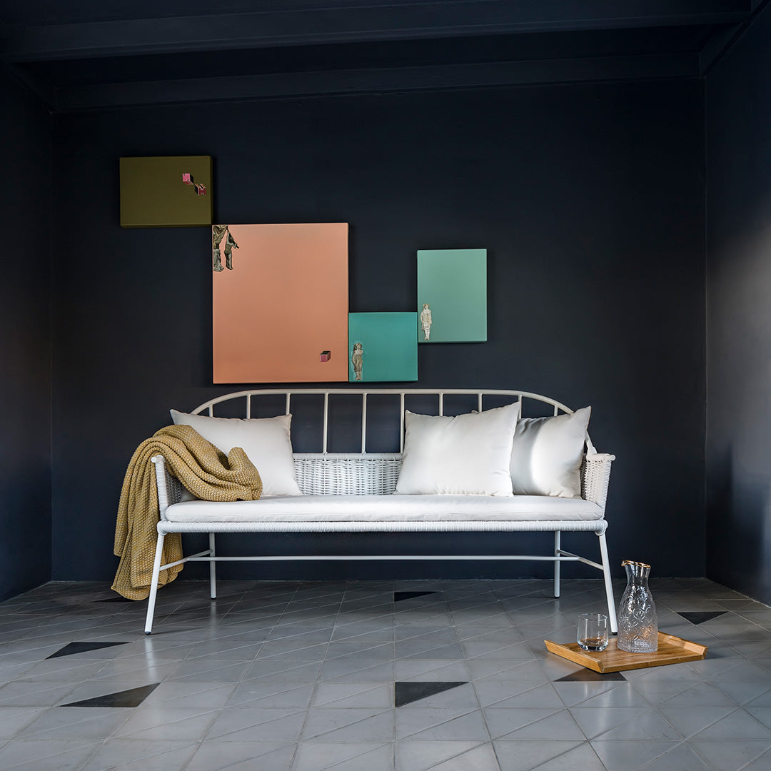 White metal bench with neutral pillows, warm beige throw, and colorful geometric wall art against a dark background.