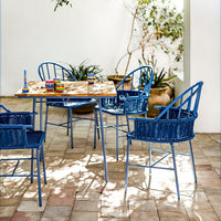 Stylish blue outdoor dining set with patterned wooden table and woven chairs, featuring a bright, inviting design.