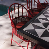 Red woven chairs and a black-and-white geometric patterned table by a poolside. Perfect for outdoor dining.