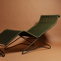 Green woven lounge chair with sleek black metal frame against a warm brown background. Stylish and modern design.