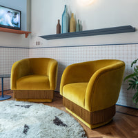 Yellow velvet armchairs with fringed bases, set against a patterned wall and wooden floor, complemented by a soft rug.