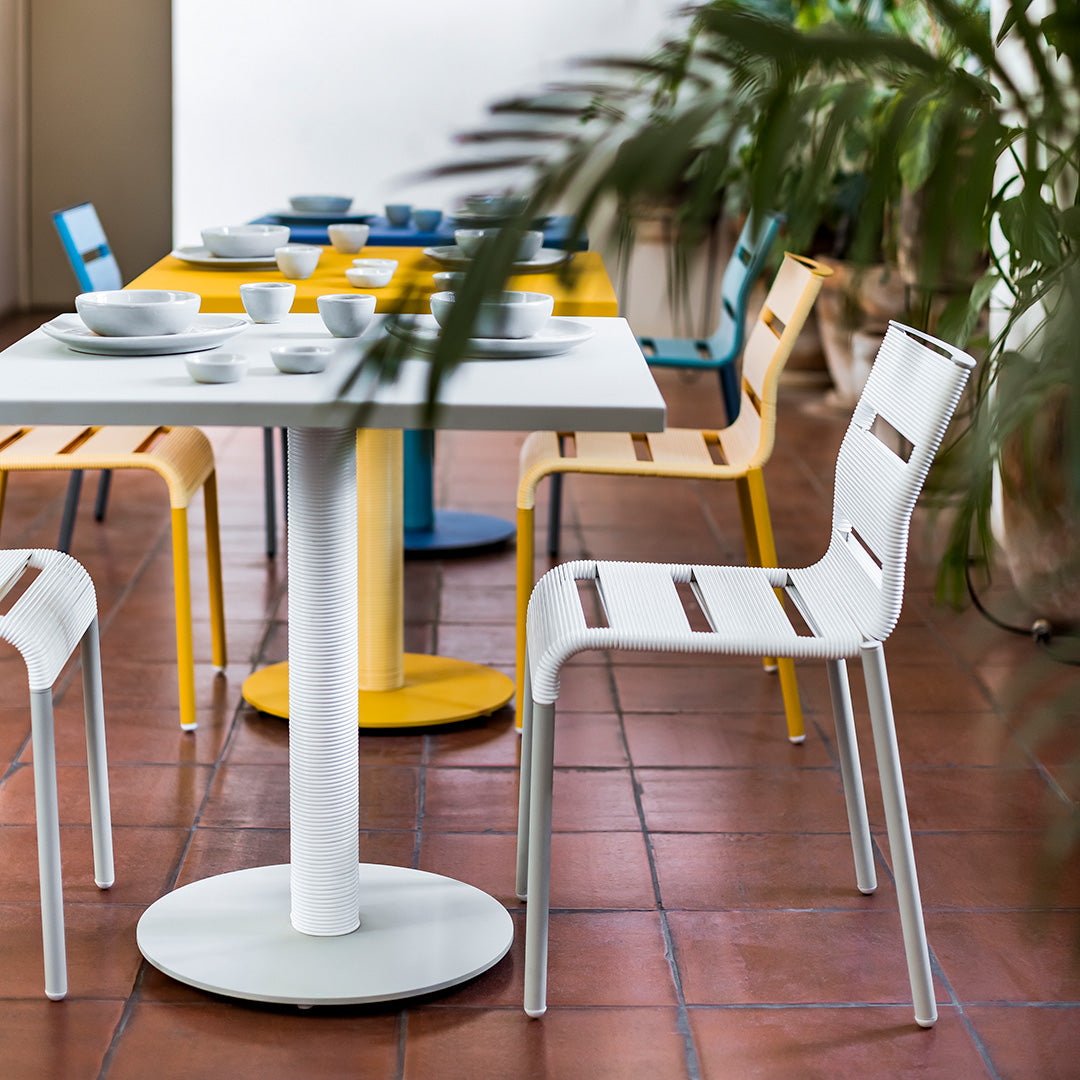 Colorful dining set featuring a white round table, yellow and blue chairs, and a modern striped pattern.
