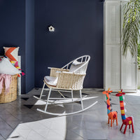 Cozy rocking chair in white, colorful geometric cushions, and vibrant patterned giraffe decor against navy blue walls.