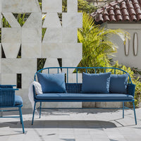 Blue metal outdoor sofa with blue cushions against a textured white wall. Modern, stylish, and vibrant patio decor.