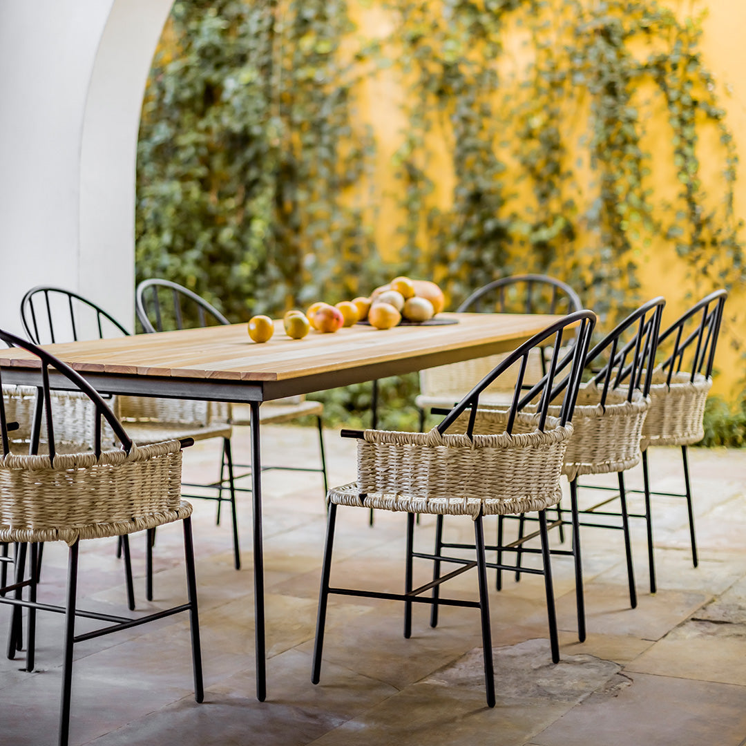 "Natural wood dining table with black metal frame and woven beige chairs, set against a vibrant yellow wall."