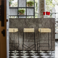 Black and white checkered floor with gray marble bar, featuring three straw-top stools and red glass decor.