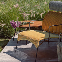 Yellow woven chair with intricate patterns, paired with a natural wood table and lush green grass backdrop.