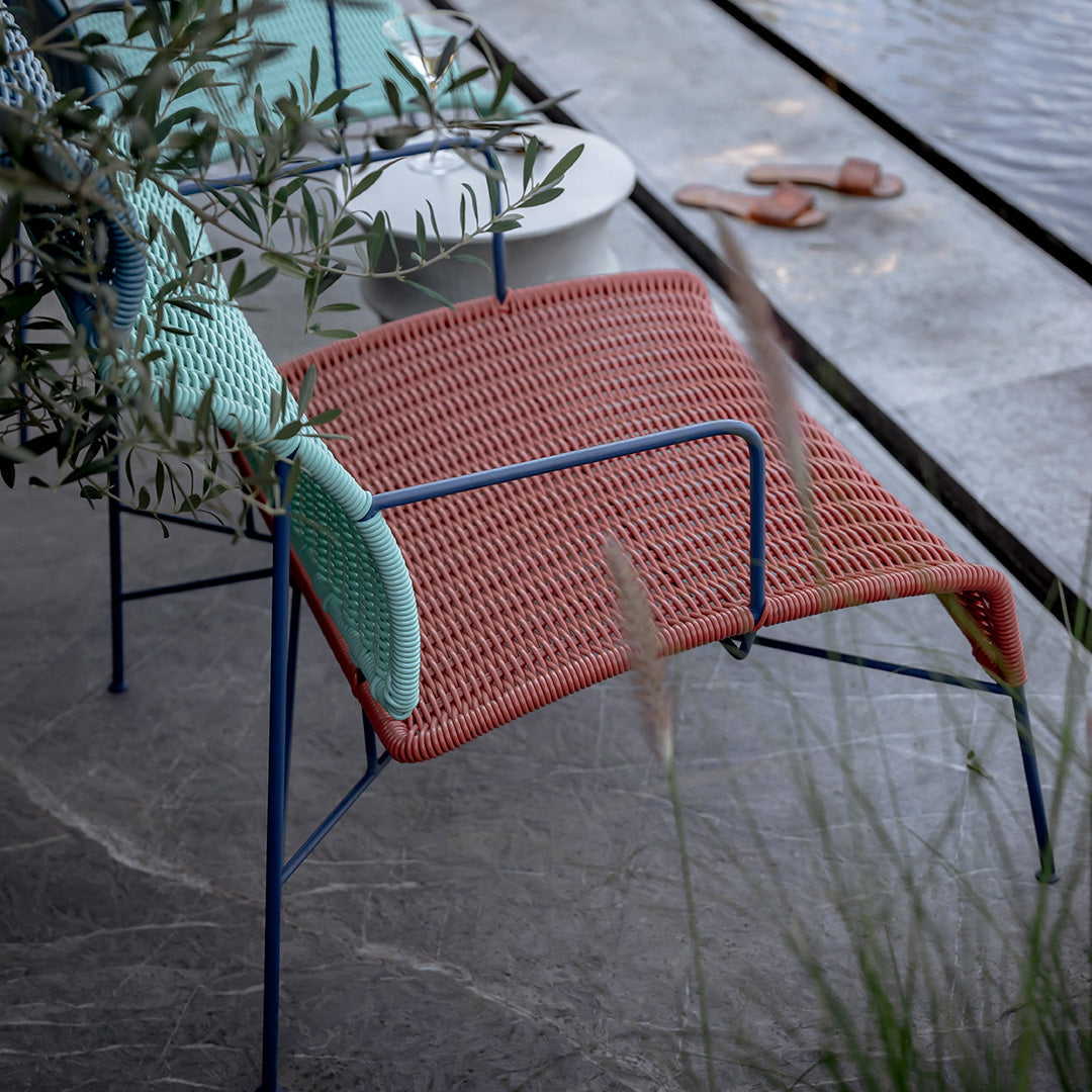 Colorful patio chair with a coral red woven seat and contrasting light mint green arms, on a stylish outdoor setting.