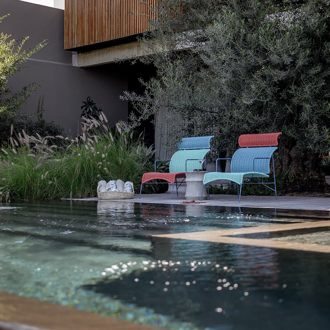 Colorful outdoor chairs in pastel shades of mint green and coral, set against a serene pool and lush greenery.
