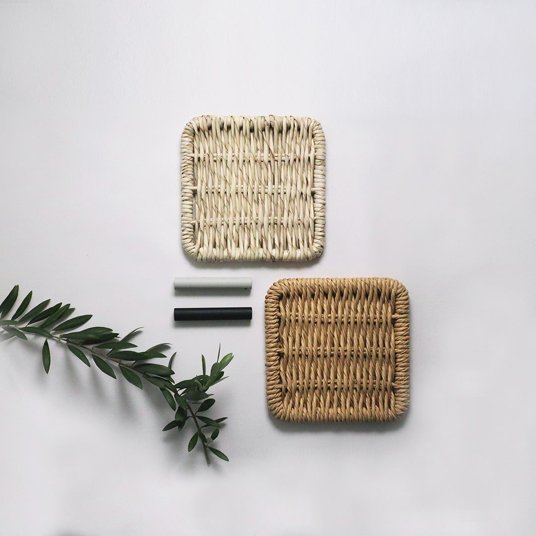 Two woven square baskets in natural and cream colors with intricate patterns, alongside decorative black and white accents.