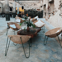 Woven rattan chairs with natural patterns, earthy tones, and modern metal legs against a textured concrete floor.