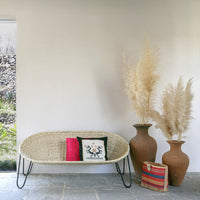 Natural wicker sofa in neutral tones, accented with vibrant pink and colorful tribal patterns, paired with earthy pots.