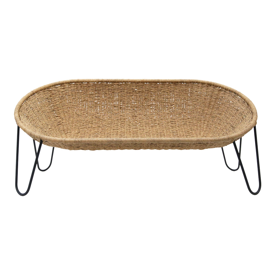 Woven natural rattan basket in oval shape with black metal legs, featuring a textured surface and earthy tones.