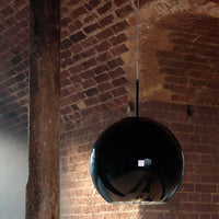 Glossy black spherical pendant light against rustic brick backdrop, featuring a minimalist design with a sleek finish.
