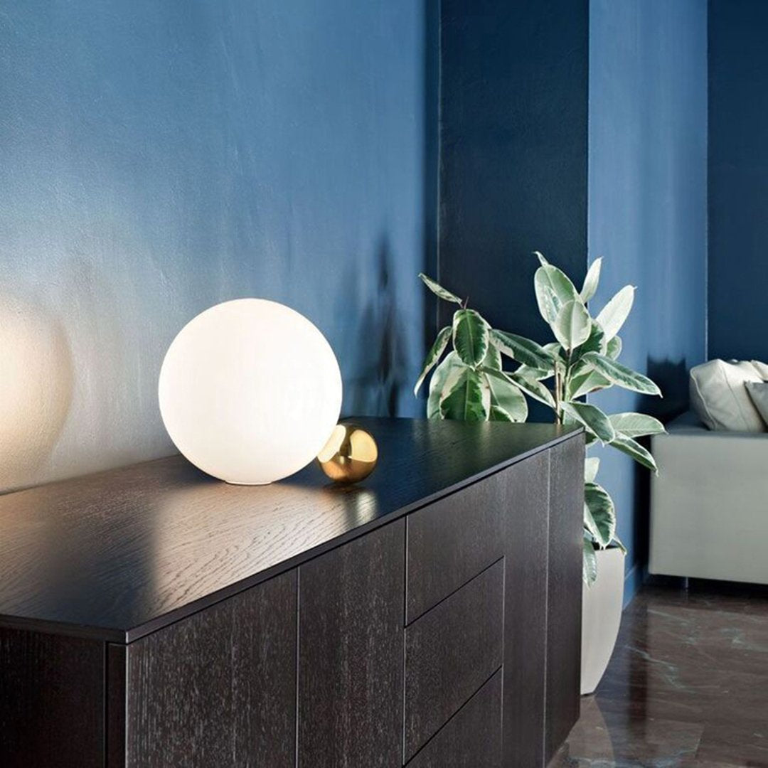"Modern interior with dark wood, white globe lamp, green plants, and rich blue walls for a stylish ambiance."