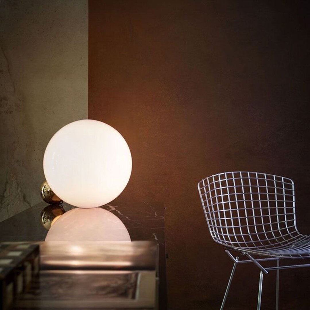 Glowing white sphere lamp against a warm brown background, complemented by a sleek wire chair.