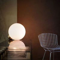 Glowing white sphere lamp against a warm brown background, complemented by a sleek wire chair.