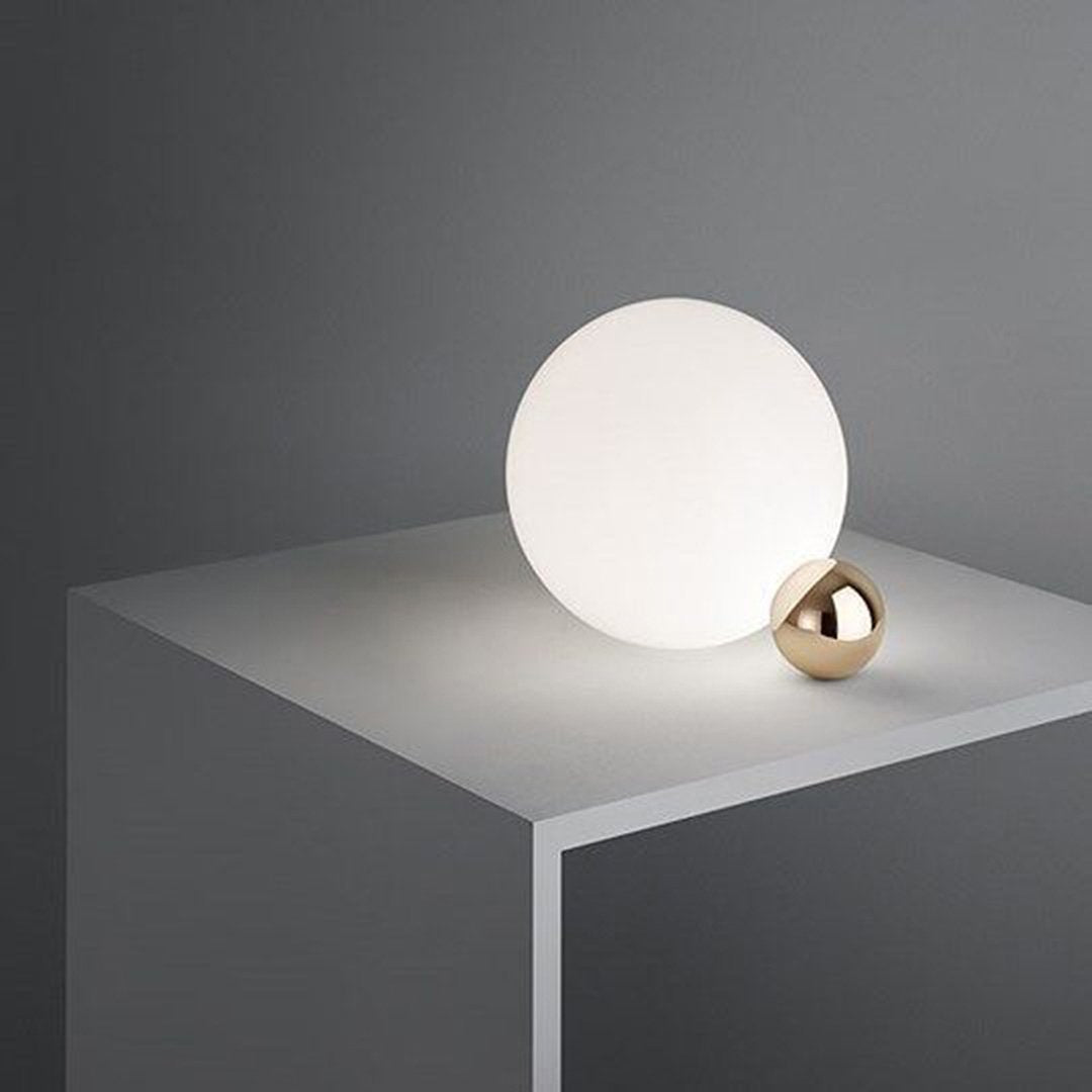 Modern table lamp featuring a smooth white circular shade and a sleek gold accent, set against a minimalist gray background.