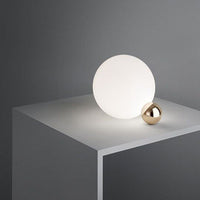 Modern table lamp featuring a smooth white circular shade and a sleek gold accent, set against a minimalist gray background.