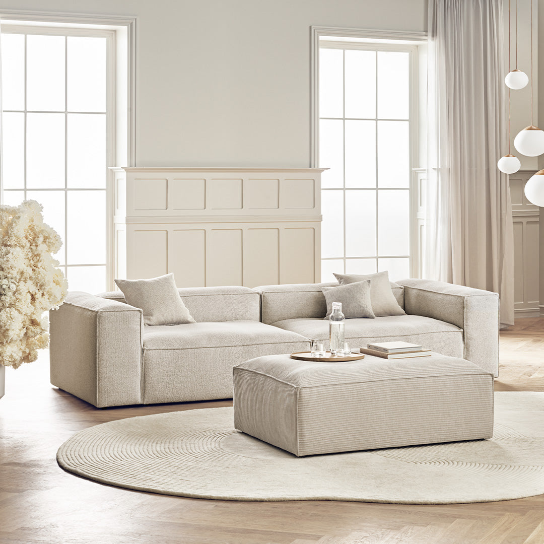 Cozy beige sectional sofa with matching ottoman, featuring a smooth, minimalist design and soft fabric texture.