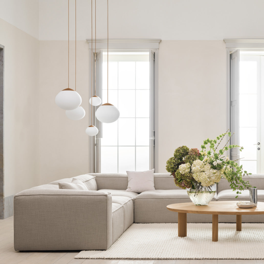 Soft beige sectional sofa, white pendant lights, and a light wood coffee table with neutral floral arrangement.