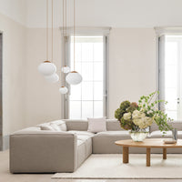 Soft beige sectional sofa, white pendant lights, and a light wood coffee table with neutral floral arrangement.