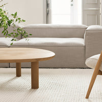 Neutral gray sofa with a textured fabric, complemented by a light wooden coffee table and a woven area rug.