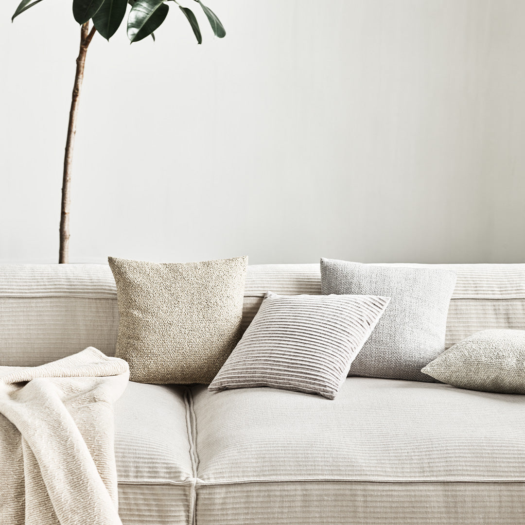 Neutral-colored throw pillows with textures and subtle patterns on a light sofa, complemented by a soft blanket.
