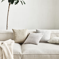 Neutral-colored throw pillows with textures and subtle patterns on a light sofa, complemented by a soft blanket.