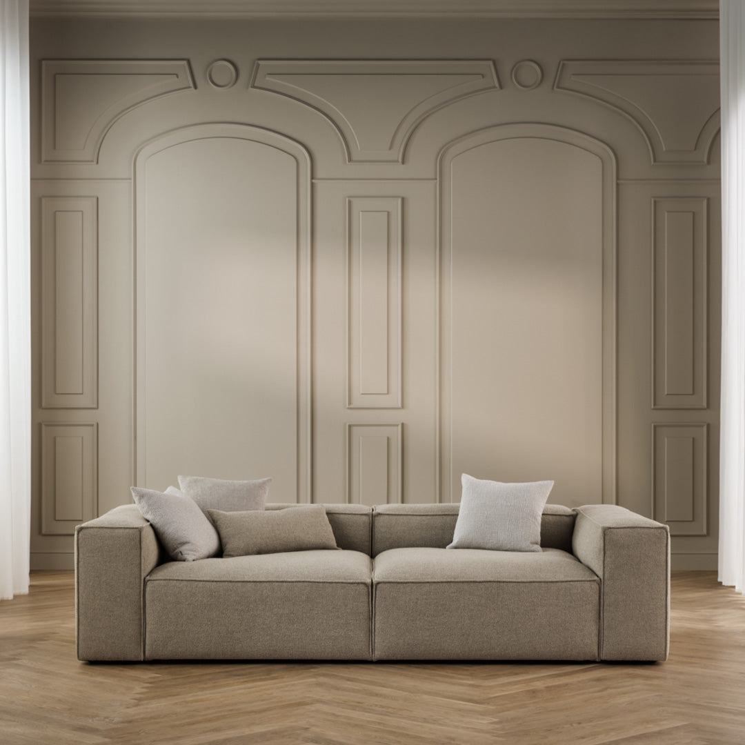 Beige modular sofa with textured fabric and minimalist design, set against a neutral wall with elegant molding.