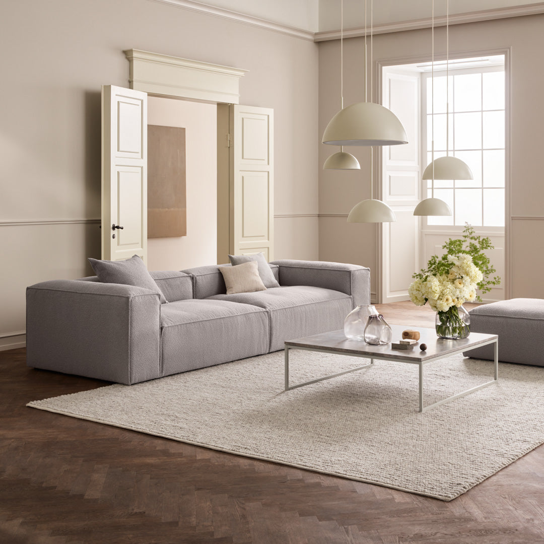Modern gray sofa with sleek lines, paired with a neutral rug and warm beige walls, creating a minimalist aesthetic.
