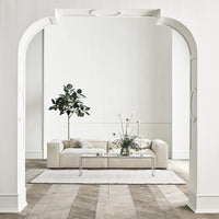 Beige sofa with soft texture, complemented by a light area rug and natural greenery against a white wall background.