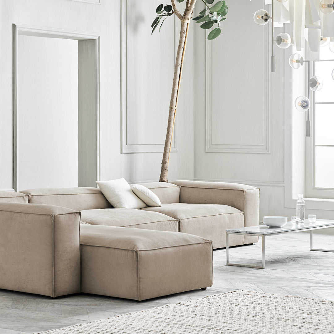 Beige modern sectional sofa with clean lines and plush cushions, paired with a light gray area rug in a contemporary setting.