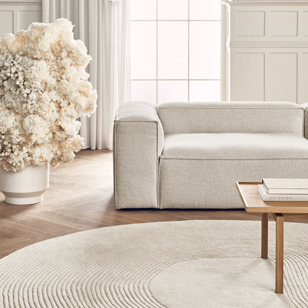 Textured light beige fabric sofa with a soft, neutral round rug and a backdrop of delicate floral decor.