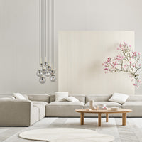 Modern beige sofa with white cushions, light gray wood floor, and soft pink floral accents. Minimalist decor style.