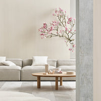Light grey sofa with white cushions, soft beige walls, and a natural wooden coffee table. Subtle floral accent.