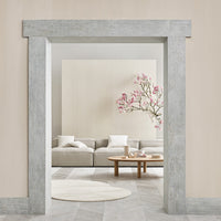 "Minimalist living room with soft beige walls, gray stone archway, lush pink floral accents, and a round white rug."