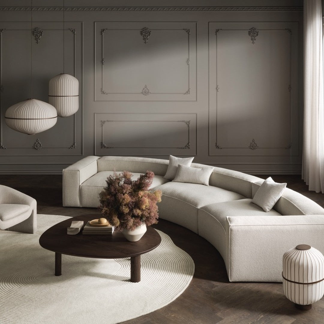 Neutral-toned curved sofa with light beige cushions, soft textures, and earthy accents in a modern living room setting.