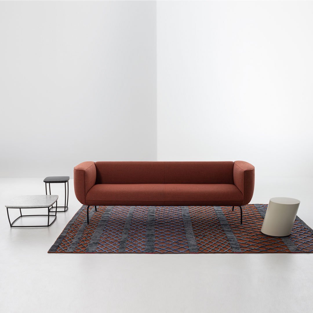 Terracotta sofa on geometric patterned rug with navy, orange, and cream tones, complemented by modern black and white tables.