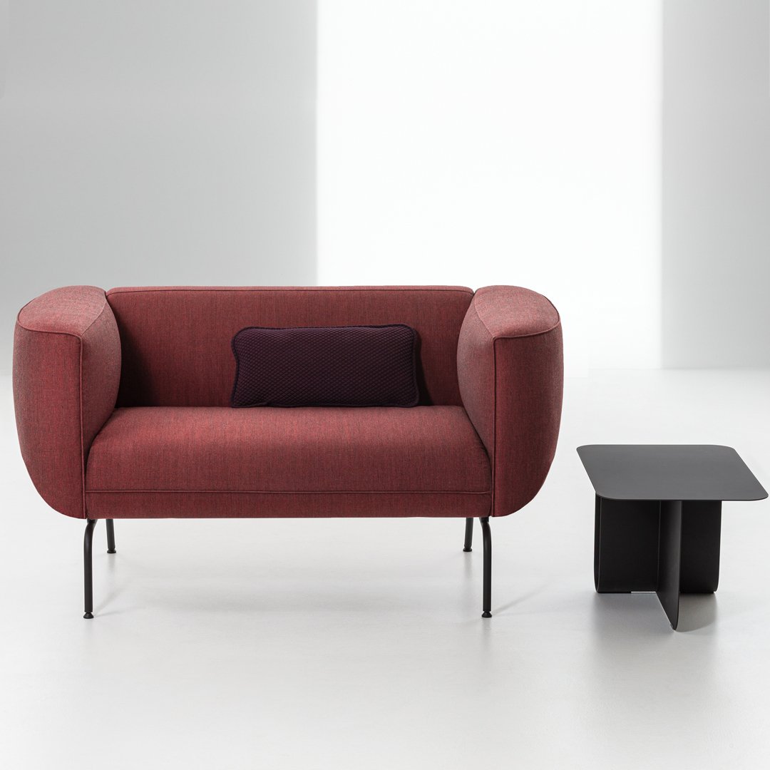 "Modern burgundy sofa with rounded arms and a dark purple accent pillow, paired with a sleek black side table."