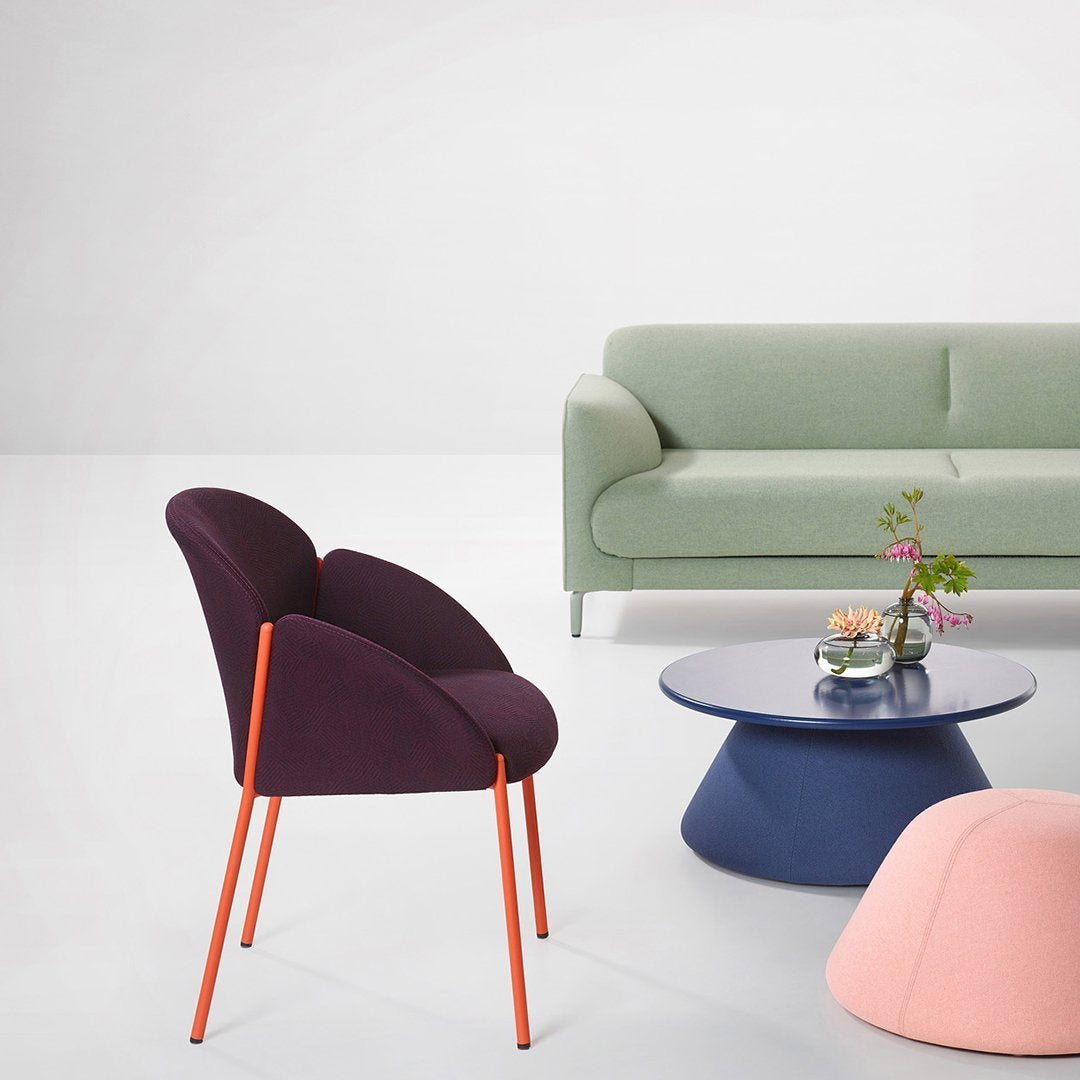 "Modern chair in purple with orange legs, green sofa, blue round table, and soft pink pouf on a light background."