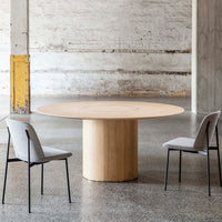 Light oak round table with a smooth finish, paired with soft gray upholstered chairs against a minimalist backdrop.
