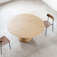 Light wood round dining table with a smooth finish, paired with a walnut chair and minimalist black legs.
