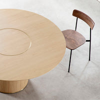 Light wood round table with smooth grain and a sleek brass accent, paired with a dark walnut chair and black metal legs.