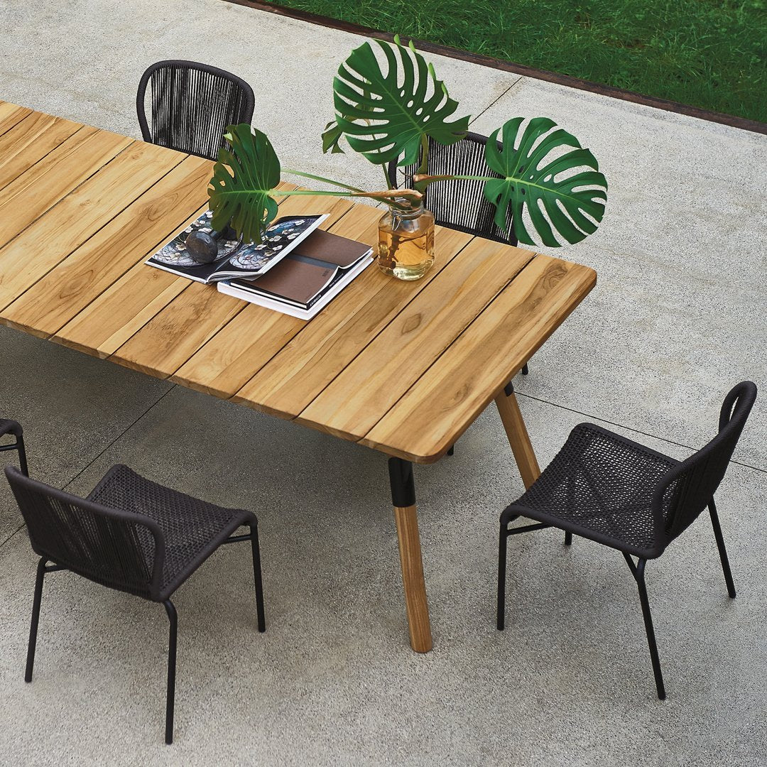 "Natural wood table with sleek black chairs and green plant accents on a textured concrete surface."